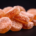 Close-up of sugar-coated watermelon gummies, orange rounds dusted in coarse sugar on a dark background