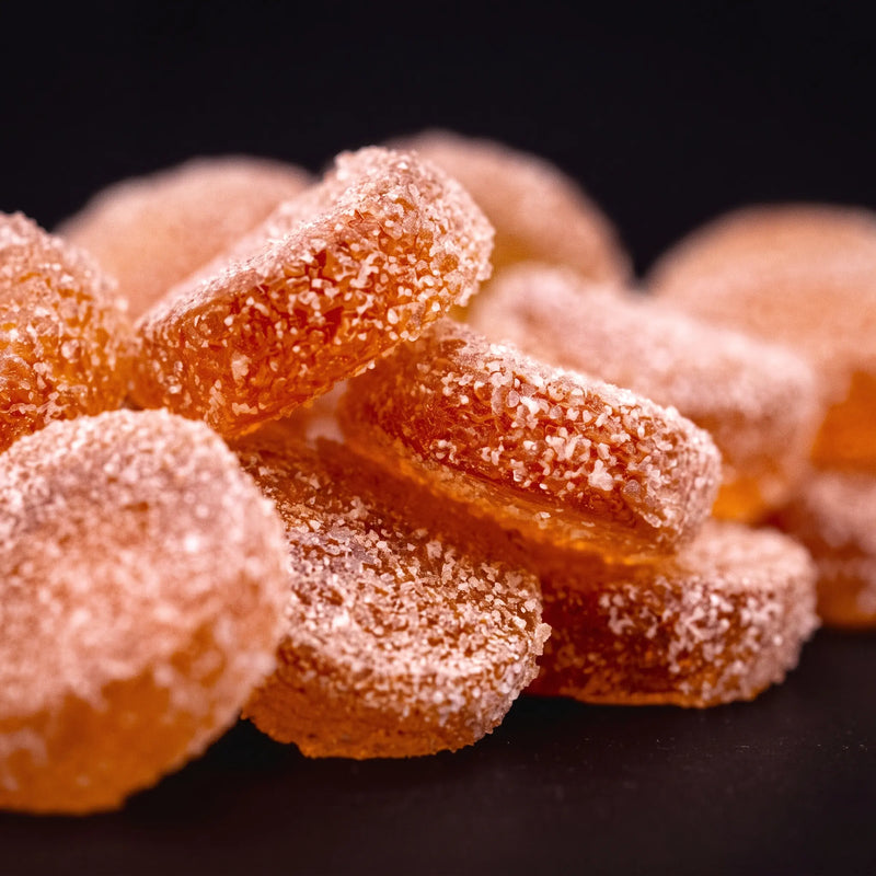 Close-up of sugar-coated watermelon gummies, orange rounds dusted in coarse sugar on a dark background