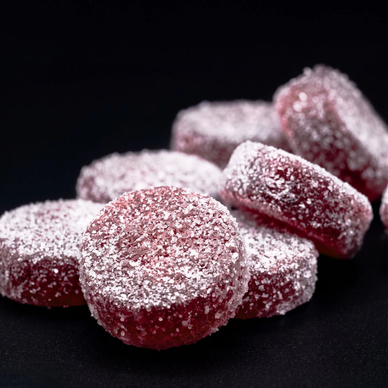 Close-up of sugar-coated grape gummies, deep purple rounds dusted in coarse sugar on a dark background