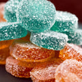 Close-up of teal and orange sour gummy candy stacked together, each round coated in coarse sugar
