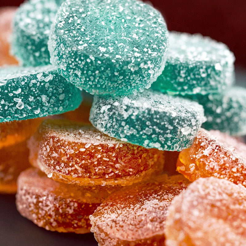 Close-up of teal and orange sour gummy candy stacked together, each round coated in coarse sugar