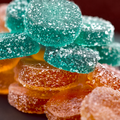 Close-up of low sugar sour gummies in teal and orange, coated in sparkling sugar crystals