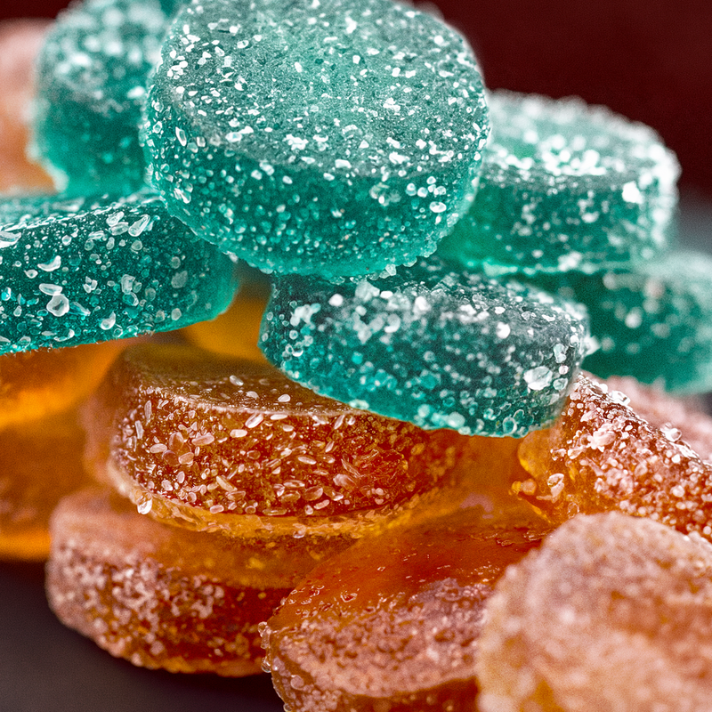 Close-up of low sugar sour gummies in teal and orange, coated in sparkling sugar crystals